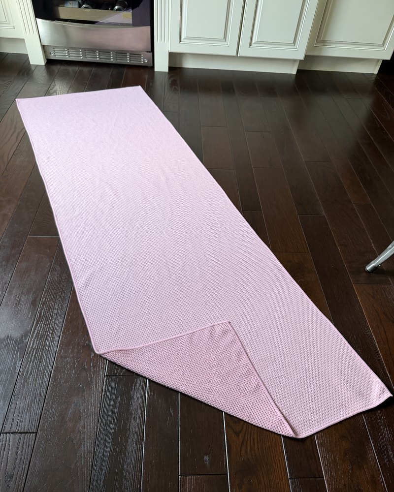 Phone photo of a pink pilates towel laid flat on a dark wood floor.